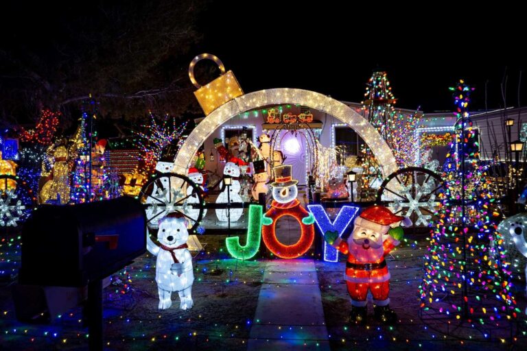 Colorful Christmas yard display with glowing “JOY” sign, Santa, polar bears, snowmen, and bright holiday lights.