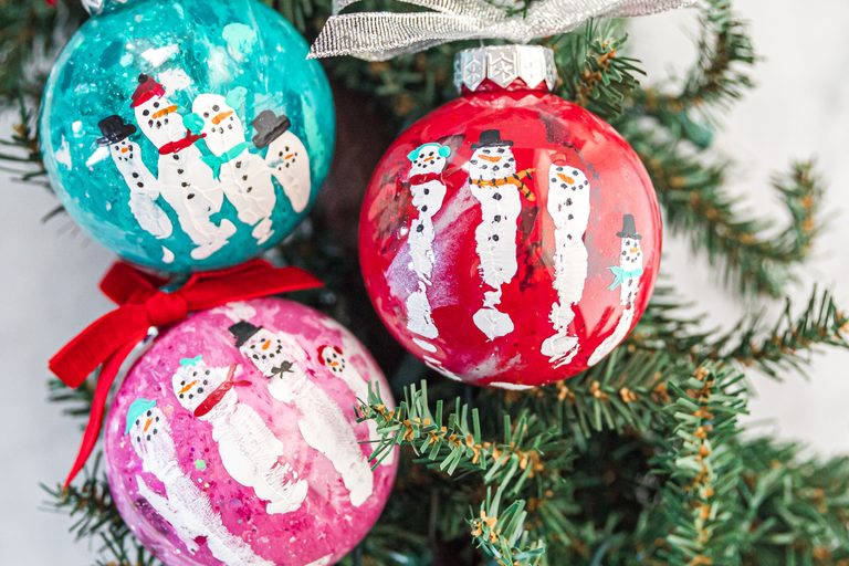 Colorful snowman handprint Christmas ornaments on a Christmas tree.